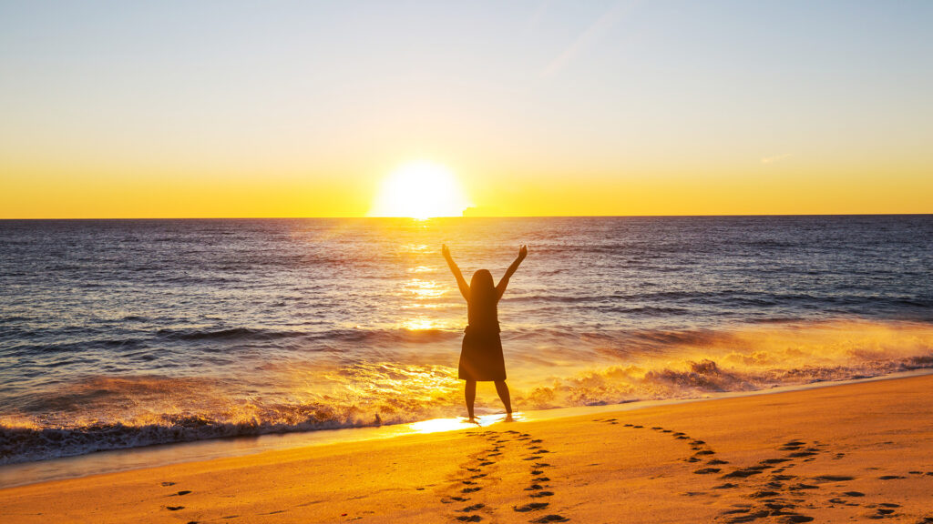 Picture of a woman on the beach raising her hands in praise