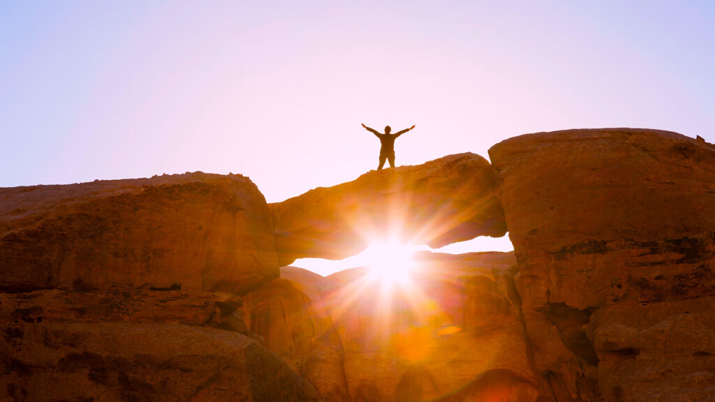 Picture of person with arms raised in air on top of natural land brigde